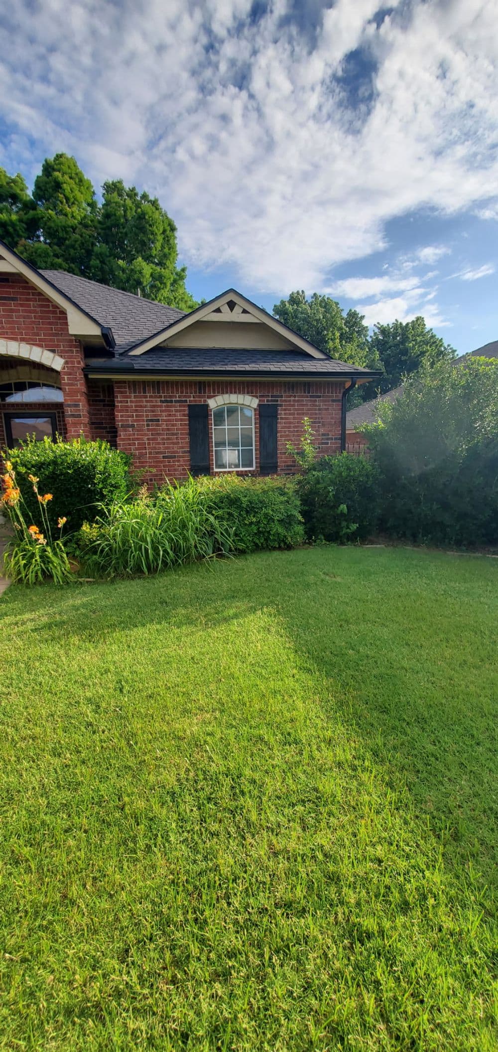 Brick house with well-maintained lawn and lush greenery under a blue sky.